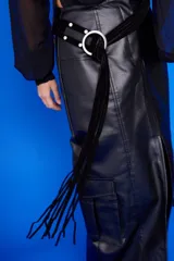 Cinturón negro de cuero con hebilla metálica plateada en forma de aro. El cinturón se anuda y tiene una tira de gamuza negra con flecos colgantes.