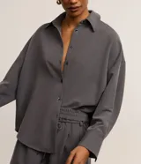 Camisa gris de tejido plano con corte sastre, cuello clásico, abotonada en el frente y puños largos.