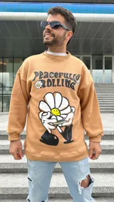 Buzo color beige con cuello redondo, puños y cintura acanalados. Estampado frontal con la frase "Peacefully Rolling" y un dibujo de una flor con una cara sonriente.