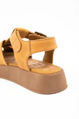 Sandalia tipo guillermina de cuero color camel, con diseño de tiras anchas entrelazadas, cierre con hebilla metálica lateral y suela de plataforma plana en tono marrón.