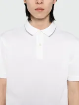 Polo de pique BOSS de color blanco, de manga corta, con cuello y puños acanalados que presentan detalles en contraste. Cuenta con cierre frontal de botones.