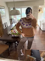 Sweater tejido a mano en mohair, de color marrón con diseño de canesú estampado con corazones fucsias y detalles geométricos en tonos beige y rosado. Presenta cuello redondo y mangas largas.