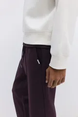Jogger color bordó en tejido suave de mezcla de algodón, con pliegue cosido en la parte delantera. Presenta cintura elástica con cordón ajustable, bolsillos laterales y un bolsillo insertado en la parte trasera.