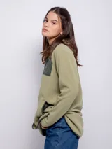Campera polar color verde oliva, de corte largo, con cuello alto y cierre frontal. Tiene un bolsillo de nylon verde oscuro en el pecho y dos bolsillos laterales.