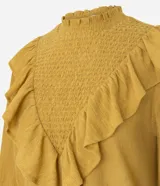 Blusa de manga larga color mostaza con cuello alto y detalle de panel delantero texturizado. Presenta volados aplicados en el busto y puños abotonados.