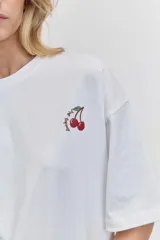 Remera blanca de corte oversize con cuello redondo y mangas cortas, presenta un pequeño bordado de cerezas en el pecho.