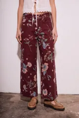 Jean de corte wide leg con tiro medio, confeccionado en algodón peinado. Presenta un diseño estampado con motivos florales sobre una base de color bordó.