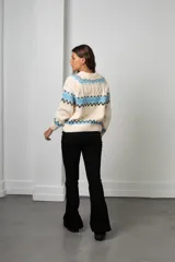 Buzo de tejido de punto con diseño nórdico, cuello redondo acanalado y mangas largas. Presenta un patrón geométrico en tonos celeste, negro y crema.