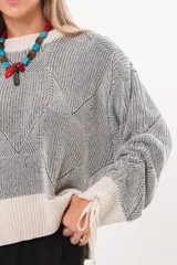 Buzo tejido de punto bicolor en tonos crudo y gris, con silueta relajada, mangas amplias con jaretas regulables en los puños y cuello redondo.