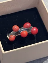 Anillo artesanal de vidrio transparente con diseño irregular y esferas decorativas de color rojo.