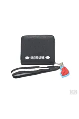 Billetera tipo monedero de cuero sintético negro con parche frontal blanco que incluye el texto 'MON AMOUR' y logo de la marca. Incluye una correa de muñeca a rayas y un dije colgante en forma de labios rojos.