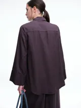 Camisa de corte oversize color bordó, con cuello clásico, cierre frontal de botones y mangas largas amplias con puños anchos. Presenta un diseño de caída fluida con bajo redondeado y levemente más largo en la parte posterior.