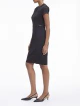 Vestido negro de corte ajustado, con largo a la rodilla, mangas cortas y cuello redondo. Presenta un cierre de cremallera en la parte posterior y recortes en los hombros.