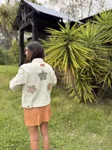 Campera de jean marrón suave con apliques de flores de crochet en el pecho, costuras decorativas artesanales en cuello y bordes, bolsillos frontales y cierre con botones.