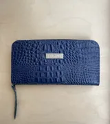 Billetera de mano con cierre, color rojo charol, con textura símil cocodrilo y logo metálico de la marca Pecari.