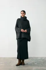 Sweater tipo poncho de tejido grueso en color gris oscuro, con cuello alto tipo polera y mangas anchas. Presenta un diseño holgado y texturizado.