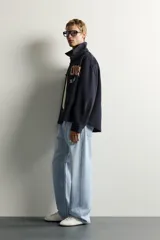 Sobrecamisa de ajuste relajado en color azul marino, con cuello de solapa, manga larga con puño abotonado y cierre frontal con botones. Presenta bordados contrastantes en el frente con la inscripción "St. Louis Worldwide Goods" en tonos naranja y blanco.