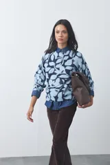 Sweater de punto con diseño estampado de hojas en tonos azul claro y azul oscuro. Presenta cuello redondo, mangas largas y terminaciones acanaladas en puños y ruedo.