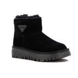 Pantubota de cuero negro con interior forrado en lana natural, suela de goma dentada y aplique triangular con logo en el lateral.