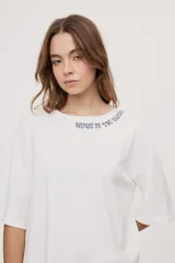 Remera de manga corta y cuello redondo, de corte oversized en color marrón, con texto bordado o estampado a lo largo del escote en el hombro izquierdo.