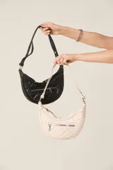 Cartera tipo baguette color crema, de ecocuero matelassé con cierre frontal y correa regulable.