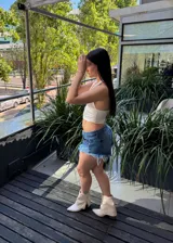 Short de denim azul con efecto desgastado, tiro medio y botamanga con flecos deshilachados.