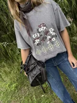 Remera de algodón gris con efecto lavado, de corte holgado y manga corta. Presenta un estampado frontal con diseño de árboles y figuras geométricas a cuadros, acompañado por la frase 'Jardín de Invierno'.