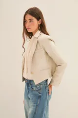 Saco corto tipo blazer en color beige, confeccionado en lino con acabado brillante. Presenta solapas clásicas, cierre frontal con un botón y mangas largas con puños abotonados.