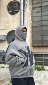 Campera con capucha gris oscura, cierre frontal y diseño oversize con doble capucha, incluyendo balaclava integrada. Presenta gran estampa contrastante en el frente.