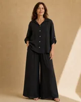 Camisa de lino negra, de corte amplio y relajado, con cuello camisero, bolsillo ojal en el pecho, mangas largas con presilla para arremangar y botones de nácar en la parte frontal.