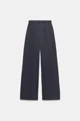 Pantalón de algodón color beige con tiro medio, cintura elástica ajustable con cordón y perneras anchas con pliegues delanteros y bolsillos laterales.