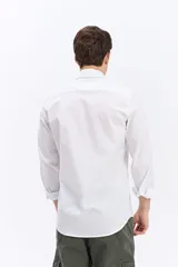 Camisa de manga larga blanca con calce semi slim, cuello camisero, cierre frontal con botones y logo bordado al tono en el pecho.