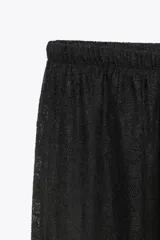 Pantalón negro de tiro alto, confeccionado en encaje transparente con diseño floral. Posee cintura elástica y bajo abullonado con elástico. Incluye forro interior tipo shorts.