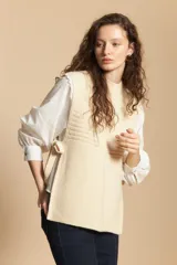 Chaleco de tejido de punto en color crema, con cuello alto y diseño acanalado. Presenta una silueta relajada con aberturas laterales.