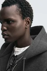 Sudadera con capucha de corte relajado confeccionada en tejido técnico con elasticidad y acabado efecto neopreno. Presenta cierre frontal de cremallera de doble dirección, bolsillos tipo canguro y terminaciones en rib.