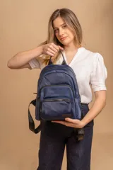 Mochila urbana de diseño funcional en color beige, confeccionada en tela impermeable. Cuenta con un compartimento principal amplio, un bolsillo secundario y un bolsillo frontal, todos con cierre. Incluye asa superior y correas ajustables para los hombros, con detalle de etiqueta de marca en el frente.