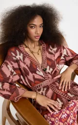 Kimono de punto Le Lis Blanc modelo Bina, con patrón jacquard geométrico en tonos rosados, marrones y crudo. Presenta escote en V profundo con ribete acanalado, mangas anchas de largo medio, corte holgado y cinturón de la misma tela para atar en la cintura.