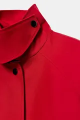 Trench largo ZARA Woman Collection de color rojo con cuello solapa, manga larga y bolsillos laterales ocultos. Presenta forro interior a contraste y cierre frontal con botones a presión.