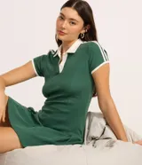 Vestido corto verde esmeralda de tejido rib, estilo skater, con cuello polo blanco y escote en V. Presenta ribetes blancos en el cuello, puños y a lo largo de las costuras laterales, simulando un look deportivo.
