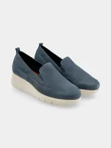 Zapatilla slip-on de mujer color azul, con plataforma tipo cuña de color crema. La capellada es de material liso y perforado en la zona del empeine.