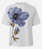 Remera de corte boxy confeccionada en algodón, con cuello redondo y mangas cortas. Presenta un estampado frontal de una flor grande en tonos violetas con detalles bordados.