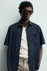 Camisa azul marino de corte regular fit confeccionada en tejido fluido de algodón y lino, con cuello solapa, manga corta, bolsillo aplicado en el pecho y cierre frontal con botones.