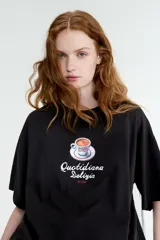 Remera oversized en punto suave de algodón de color negro con diseño estampado en el centro que muestra una taza de espresso y el texto "Quotidiana Delizia ROME". Cuenta con cuello redondo acanalado, hombros caídos y mangas cortas.