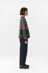 Campera tipo bomber tejida con diseño jacquard geométrico en tonos azul marino, blanco, rojo y verde. Presenta cierre frontal completo, cuello, puños y ruedo acanalados en color verde y blanco, con corte oversized y hombros caídos.