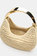 Bolso de mano mini con cuerpo trenzado en color beige y asa rígida metálica dorada. Incluye correa bandolera extraíble y cierre superior de cremallera.