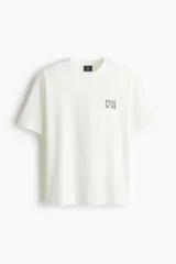 Remera de algodón blanca de corte holgado, con cuello redondo y diseño estampado en el pecho con el texto 'PALM NOIR'.