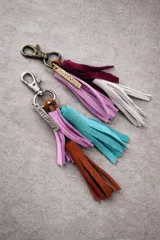 Llavero con borlas de gamuza multicolor, compuesto por un aro metálico con cierre de mosquetón y una placa metálica grabada con la marca Sierra Mora.