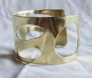 Brazalete rígido de bronce color dorado con diseño calado irregular.