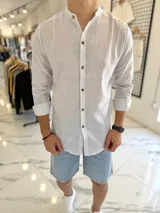 Camisa blanca con finas rayas azules, cuello mao y cierre frontal con botones marrones de efecto madera, de manga larga.