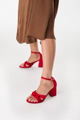 Sandalias rojas de cuero con diseño de nudo frontal, tira fina al tobillo con hebilla metálica y taco ancho estructurado.